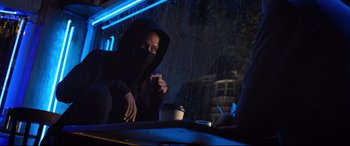 Movie still from “Death Note” (2017), directed by Adam Wingard – A person sitting at a table in the rain with a cup; Medium shot, Over the shoulder angle