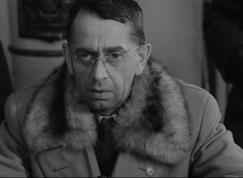 Movie still from “Closely Watched Trains” (1966), directed by Jirí Menzel – An older man wearing glasses and a fur collar; Close Up shot, Over the shoulder angle