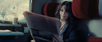 Movie still from “Clouds of Sils Maria” (2014), directed by Olivier Assayas – A woman sitting on a train reading a newspaper; Close Up shot, Over the shoulder angle