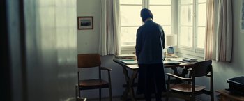 Movie still from “Clouds of Sils Maria” (2014), directed by Olivier Assayas – A woman standing at a table in front of a window; Wide shot, Over the shoulder angle