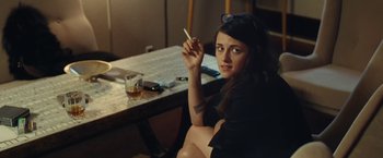Movie still from “Clouds of Sils Maria” (2014), directed by Olivier Assayas – A woman sitting at a table holding a cigarette in her hand; Medium shot, High angle