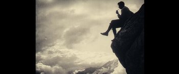Movie still from “Clouds of Sils Maria” (2014), directed by Olivier Assayas – A man sitting on top of a cliff drinking a cup; Wide shot, Low angle