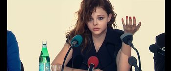Movie still from “Clouds of Sils Maria” (2014), directed by Olivier Assayas – A woman with long brown curly hair sitting in front of microphones; Close Up shot, Over the shoulder angle