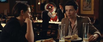 Movie still from “Clouds of Sils Maria” (2014), directed by Olivier Assayas – Two people sitting at a table in front of a plate of food; Medium shot, Over the shoulder angle