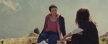 Movie still from “Clouds of Sils Maria” (2014), directed by Olivier Assayas – A woman sitting on the ground holding a card; Medium shot, Low angle