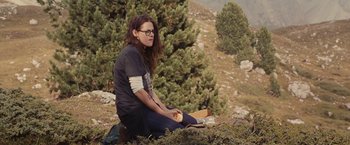 Movie still from “Clouds of Sils Maria” (2014), directed by Olivier Assayas – A woman sitting on the ground with a box in her hand; Wide shot, Over the shoulder angle