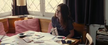 Movie still from “Clouds of Sils Maria” (2014), directed by Olivier Assayas – A woman sitting at a table with a book in her hands; Medium shot, Over the shoulder angle