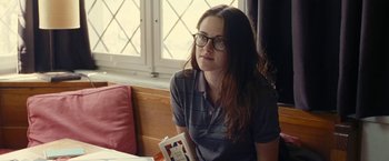 Movie still from “Clouds of Sils Maria” (2014), directed by Olivier Assayas – A woman sitting in front of a window holding a book; Medium shot, Over the shoulder angle