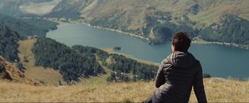 Movie still from “Clouds of Sils Maria” (2014), directed by Olivier Assayas – A man sitting on top of a hill looking at a lake; Extreme Wide shot, High angle
