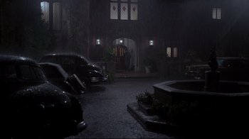 Movie still from “Clue” (1985), directed by Jonathan Lynn – A man standing in front of a building in the dark; Extreme Wide shot, High angle