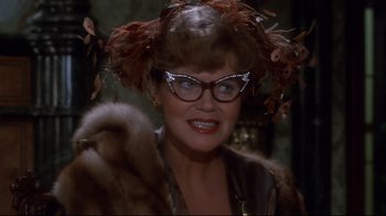 Movie still from “Clue” (1985), directed by Jonathan Lynn – A person wearing glasses and a fur coat; Close Up shot, Over the shoulder angle