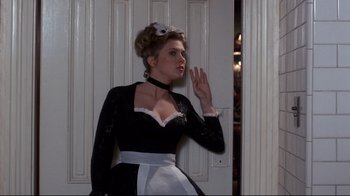 Movie still from “Clue” (1985), directed by Jonathan Lynn – A woman dressed as a french maid standing in front of a door; Medium shot, Low angle