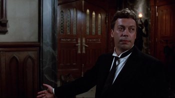Movie still from “Clue” (1985), directed by Jonathan Lynn – A man wearing a suit and tie in front of a door; Medium shot, Low angle