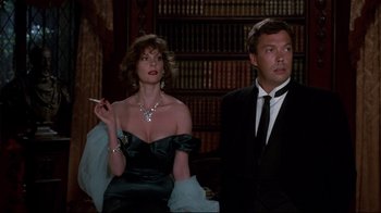 Movie still from “Clue” (1985), directed by Jonathan Lynn – A man and a woman in formal attire smoking a cigarette; Medium shot, Low angle
