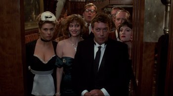 Movie still from “Clue” (1985), directed by Jonathan Lynn – A group of people standing around a man in a tuxedo; Medium shot, Low angle