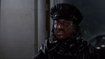 Movie still from “Clue” (1985), directed by Jonathan Lynn – A man wearing a black hat and a black jacket; Medium shot, Low angle