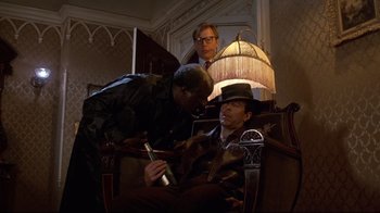 Movie still from “Clue” (1985), directed by Jonathan Lynn – A group of people sitting around a room; Medium shot, Over the shoulder angle