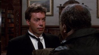 Movie still from “Clue” (1985), directed by Jonathan Lynn – A man wearing a suit and tie talking to another man wearing a suit and tie; Close Up shot, Over the shoulder angle