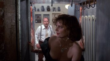 Movie still from “Clue” (1985), directed by Jonathan Lynn – A woman standing in front of a man in a room; Medium shot, Over the shoulder angle