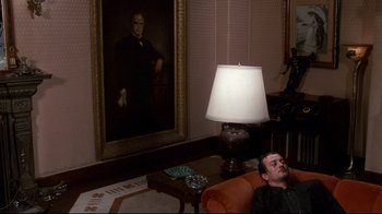 Movie still from “Clue” (1985), directed by Jonathan Lynn – A man laying on a couch next to a lamp; Wide shot, Low angle