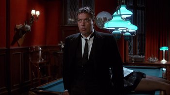 Movie still from “Clue” (1985), directed by Jonathan Lynn – A man in a suit and tie standing in front of a pool table; Medium shot, Low angle