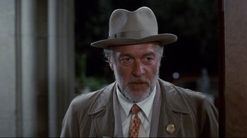 Movie still from “Clue” (1985), directed by Jonathan Lynn – An older man wearing a hat and a tie; Close Up shot, Over the shoulder angle