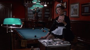 Movie still from “Clue” (1985), directed by Jonathan Lynn – A woman sitting in front of a billiards table; Medium shot, Low angle