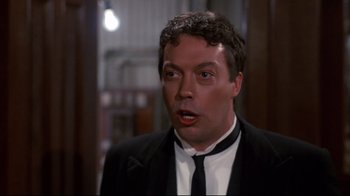 Movie still from “Clue” (1985), directed by Jonathan Lynn – A person wearing a suit and a tie; Close Up shot, Over the shoulder angle