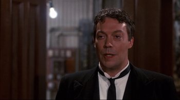 Movie still from “Clue” (1985), directed by Jonathan Lynn – A person wearing a suit and a tie; Close Up shot, Over the shoulder angle