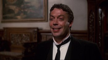 Movie still from “Clue” (1985), directed by Jonathan Lynn – A man wearing a suit and tie smiling for the camera; Close Up shot, Low angle