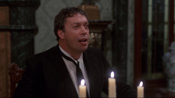 Movie still from “Clue” (1985), directed by Jonathan Lynn – A man wearing a suit and tie next to two lit candles; Medium shot, Over the shoulder angle
