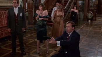 Movie still from “Clue” (1985), directed by Jonathan Lynn – A group of people standing in a room with a man holding a cell phone; Wide shot, Over the shoulder angle