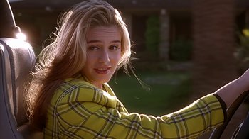 Movie still from “Clueless” (1995), directed by Amy Heckerling – A woman in a yellow plaid shirt smiling for the camera; Close Up shot, Over the shoulder angle