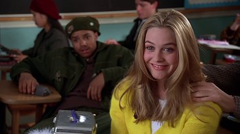Movie still from “Clueless” (1995), directed by Amy Heckerling – A woman in a yellow jacket smiles at the camera; Medium shot, High angle