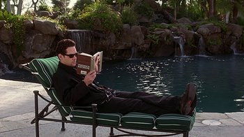 Movie still from “Clueless” (1995), directed by Amy Heckerling – A man reading a book while sitting on a lounge chair; Medium shot, High angle