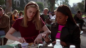 Movie still from “Clueless” (1995), directed by Amy Heckerling – Two women sitting at an outdoor table eating food; Medium shot, High angle