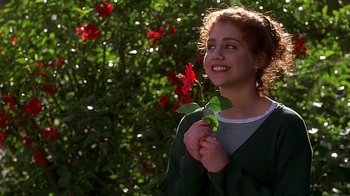 Movie still from “Clueless” (1995), directed by Amy Heckerling – A woman holding a red rose in front of some bushes; Close Up shot, Low angle