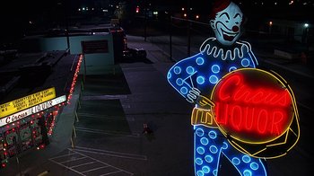 Movie still from “Clueless” (1995), directed by Amy Heckerling – A neon sign of a clown in a parking lot at night; Extreme Wide shot, Low angle