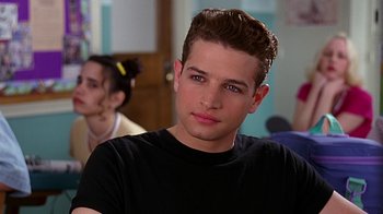 Movie still from “Clueless” (1995), directed by Amy Heckerling – A young man in a black t - shirt is looking at the camera; Close Up shot, Over the shoulder angle