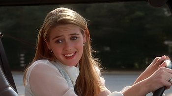 Movie still from “Clueless” (1995), directed by Amy Heckerling – A woman sitting in a car smiling for the camera; Close Up shot, Over the shoulder angle