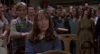 Movie still from “Coal Miner's Daughter” (1980), directed by Michael Apted – A woman sitting in front of a group of people in a room; Medium shot, Over the shoulder angle