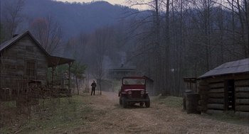 Movie still from “Coal Miner's Daughter” (1980), directed by Michael Apted – A man standing next to a red jeep on a dirt road; Extreme Wide shot, High angle