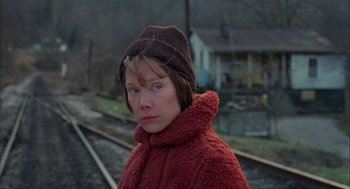 Movie still from “Coal Miner's Daughter” (1980), directed by Michael Apted – A woman wearing a red coat and a brown hat standing on train tracks; Close Up shot, Low angle
