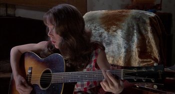 Movie still from “Coal Miner's Daughter” (1980), directed by Michael Apted – A woman playing a guitar while sitting on a couch; Medium shot, High angle