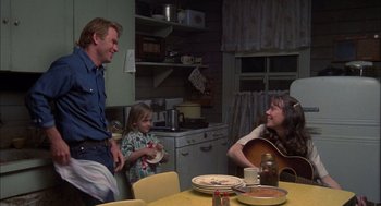 Movie still from “Coal Miner's Daughter” (1980), directed by Michael Apted – A man and a woman sitting at a table with a child; Medium shot, Over the shoulder angle