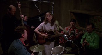 Movie still from “Coal Miner's Daughter” (1980), directed by Michael Apted – A woman playing a guitar in front of a group of people; Medium shot, High angle