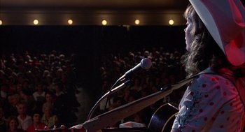 Movie still from “Coal Miner's Daughter” (1980), directed by Michael Apted – A woman is speaking at a microphone in front of an audience; Medium shot, Low angle