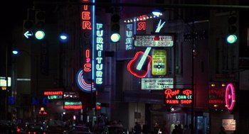 Movie still from “Coal Miner's Daughter” (1980), directed by Michael Apted – A group of people walking down a street next to neon signs; Wide shot, High angle