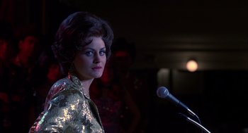 Movie still from “Coal Miner's Daughter” (1980), directed by Michael Apted – A woman in a gold jacket standing in front of a microphone; Close Up shot, Over the shoulder angle