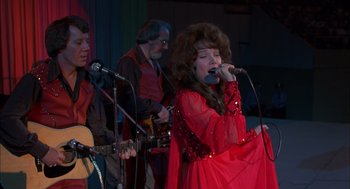 Movie still from “Coal Miner's Daughter” (1980), directed by Michael Apted – A woman in a red dress singing into a microphone; Medium shot, Low angle
